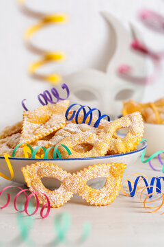 Angel wings or sfrappole or chiacchiere in shape of carnival mask. Traditional sweet crisp pastry deep-fried and sprinkled with sugar. Carnival food. Decorated with paper serpentine. Vertical image.