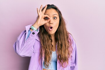 Young hispanic girl wearing casual clothes doing ok gesture shocked with surprised face, eye looking through fingers. unbelieving expression. - obrazy, fototapety, plakaty