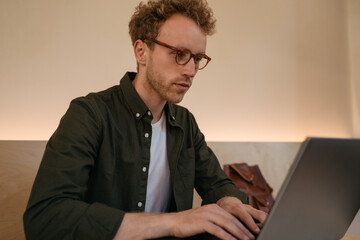 Portrait of pensive programmer using laptop computer working online from home. Young man copywriter...