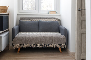 Gray soft sofa with 2 pillows. Modern design sofa in 70th style near window in an small empty room. Copy space.