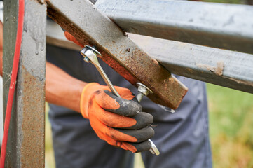Close up of man hand in work glove tightening bolt with stainless steel wrench. Male worker using wrench tool while installing metal rails for solar panel system.