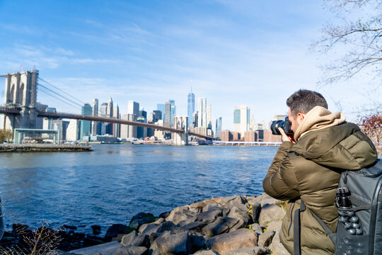 NEW YORK CITY MAN TAKING PICTURES OF MANHATTAN VIEW FROM BROOKLYN PARK LIVING HAPPY DURING WINTER TIME IN UNITED STATES. TRAVEL, SUNNY DAY AND AMERICA CONCEPT.