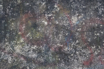 Old chipped concrete wall with multicolored paint and graffiti. Full frame image of rough shabby surface. Abstract grunge wallpaper, texture or background, copy space