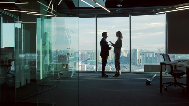 silhouette of meeting business partners in modern office room on standing near window background. Indoor. Asian man shakes hands with woman handshaking. Two businessmen talking negotiating discussion