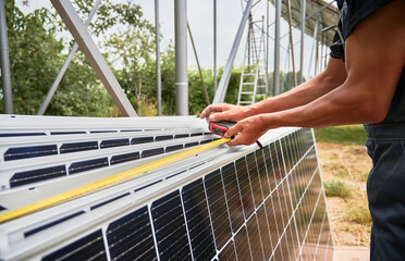 Close up of man hands measuring photovoltaic solar panels with tape measure. Male worker taking...