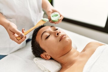 Young hispanic woman having aloe vera facial treatment at beauty center