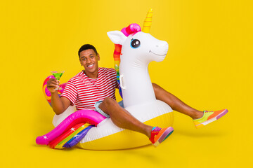Full size photo of guy swim water unicorn ring enjoy punch wear red striped t-shirt isolated over yellow bright color background © deagreez