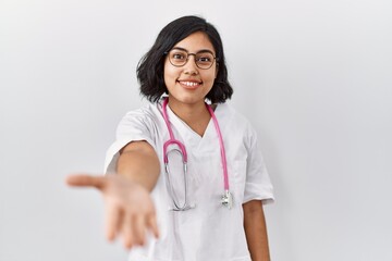 Young hispanic doctor woman wearing stethoscope over isolated background smiling friendly offering handshake as greeting and welcoming. successful business.