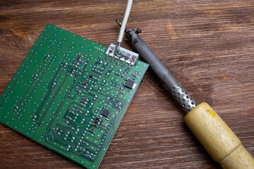 next to the green chip on the wooden table is a soldering iron