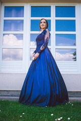 Beautiful girl in glamorous ultramarine dress standing by the window.