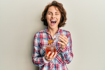 Young brunette woman holding fresh honey smiling and laughing hard out loud because funny crazy joke.