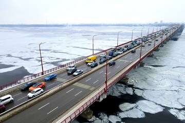 Many cars drive over river bridge in winter. Traffic jam at rush hour, air pollution, smog on...