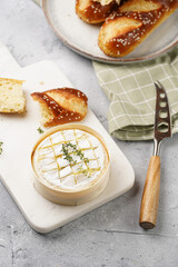Oven baked camembert cheese with lye baguette bread on marble board, grey concrete surface....