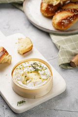 Oven baked camembert cheese with lye baguette bread on marble board, grey concrete surface. Homemade grilled brie with thyme on green checkered kitchen towel