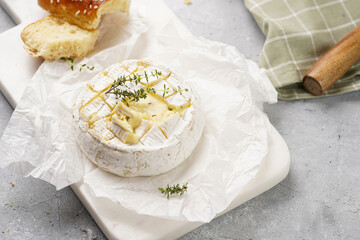 Oven baked camembert cheese with lye baguette bread on marble board, grey concrete surface....
