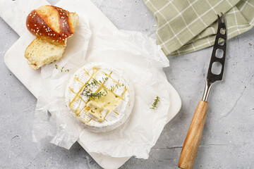 Oven baked camembert cheese with lye baguette bread on marble board, grey concrete surface....