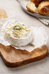 Oven baked camembert cheese with lye baguette bread on wooden board, grey concrete surface....