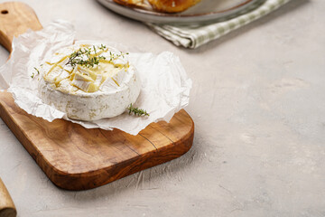 Oven baked camembert cheese with lye baguette bread on wooden board, grey concrete surface....
