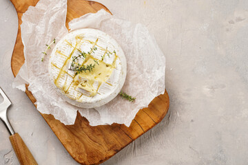 Oven baked camembert cheese with lye baguette bread on wooden board, grey concrete surface. Homemade grilled brie with thyme, rustic style table setting - obrazy, fototapety, plakaty