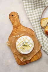 Oven baked camembert cheese with lye baguette bread on wooden board, grey concrete surface....