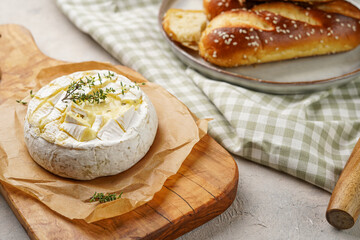 Oven baked camembert cheese with lye baguette bread on wooden board, grey concrete surface. Homemade grilled brie with thyme, rustic style table setting