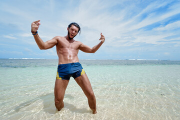 Happy vacation. Young excited man with rised hands on tropical beach.