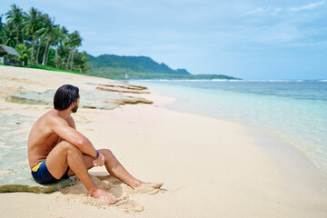 Fototapeta na wymiar Enjoying suntan and vacation.Young bearded man ralaxing on the tropical sand beach.