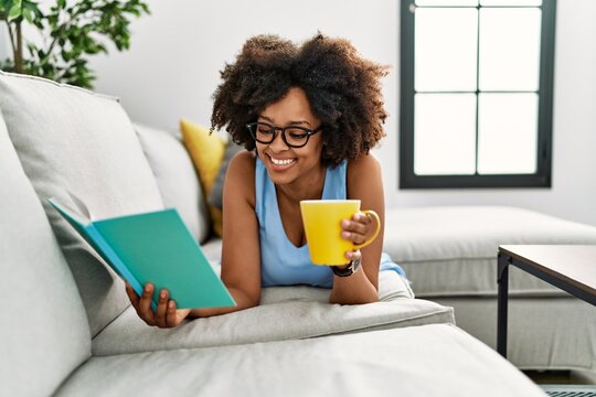 Young african american woman drinking coffee reading book at home