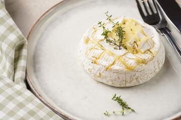 Oven baked camembert cheese with lye baguette bread on white plate, grey concrete surface. Homemade...