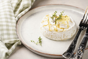 Oven baked camembert cheese with lye baguette bread on white plate, grey concrete surface. Homemade...