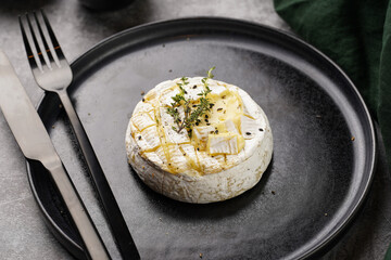 Oven baked camembert cheese with black pepper, sesame seeds on black plate, grey concrete surface....