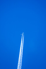 twin engine jet airliner in deep blue sky with vapour (contrails) trails vertical in the frame