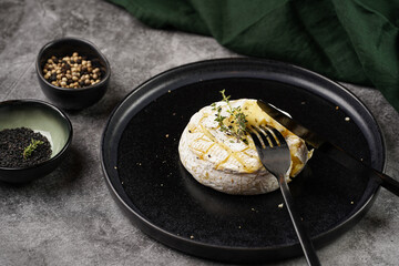 Oven baked camembert cheese with black pepper, sesame seeds on black plate, grey concrete surface....