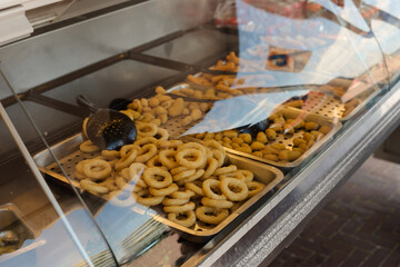 Cafeteria take-out food in showcase window. Many Fried onion rings Sitting in Showcase Display of a Fast-Food. Cafeteria tray with  fast food.