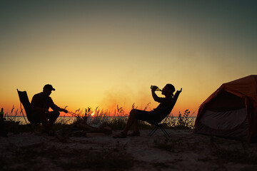 Silhouette of happy young friends resting by the bonfire near tent.