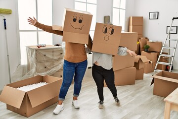 Mature mother and down syndrome daughter moving to a new home, standing wearing cardboard boxes...