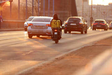 Kurier na skuterze jedzie mostem Grunwaldzkim we Wrocławiu, pod zachodzące słońce.