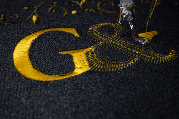 Machine embroidery on black velvet fabric with yellow thread. Embroidered initial G. Close up.	