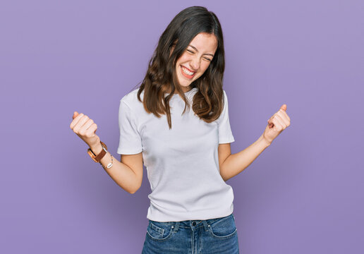 Young beautiful woman wearing casual white t shirt very happy and excited doing winner gesture with arms raised, smiling and screaming for success. celebration concept.