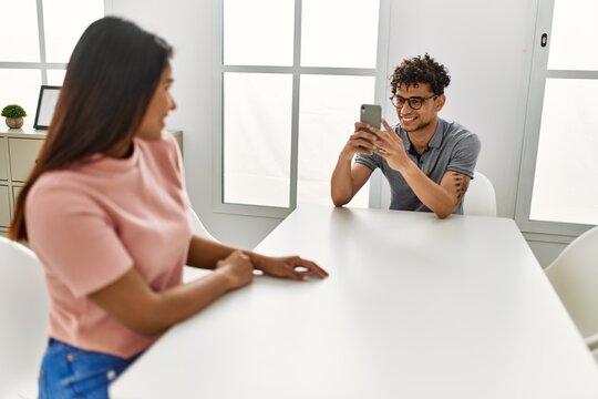 Young latin man making woman picture using smartphone at home.