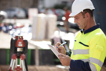 a contractor writing on clipboard stood beside theodolite