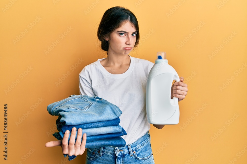 Canvas Prints Young caucasian woman doing laundry holding detergent bottle and folded jeans depressed and worry for distress, crying angry and afraid. sad expression.