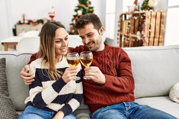 Young hispanic couple smiling happy toasting with champagne sitting on the sofa at home.
