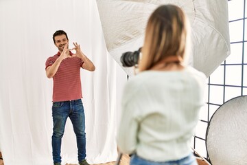 Woman photographer talking pictures of man posing as model at photography studio smiling in love showing heart symbol and shape with hands. romantic concept.