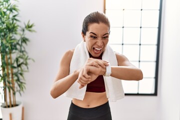 Young hispanic woman wearing sportswear looking stopwatch at sport center angry and mad screaming...