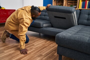Young african american man looking for something under sofa at home
