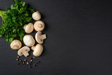 Obraz na płótnie Canvas Raw champignons wole and halved and bunch of parsley over black slate slab. Cooking fresh button mushrooms Agaricus bisporus. Vegetarian menu. Recipe with vegetable protein. Copy space.