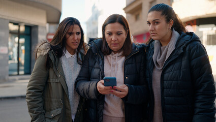 Mother and daugthers using smartphone standing together at street