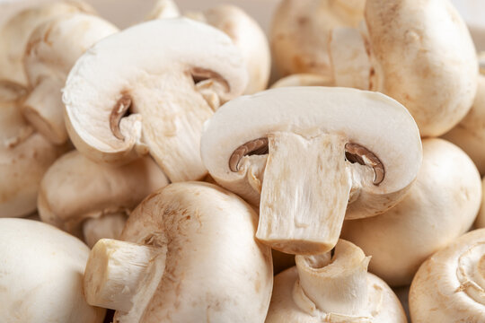 Halved raw champignon and whole button mushrooms. Cultivated white mushrooms background. Agaricus bisporus widely cultivated in the world. Vegetable protein. Vegetarian food. Dieting.