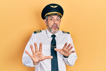 Handsome middle age man with grey hair wearing airplane pilot uniform afraid and terrified with fear expression stop gesture with hands, shouting in shock. panic concept. © Krakenimages.com